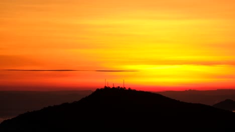 Silhouette-of-radio-towers-on-mountain-top-against-vibrant-sunset-background
