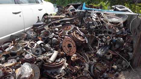 Pile-of-waste-scrap-metal-car-parts-next-to-junk-white-pickup-truck-in-scrapyard