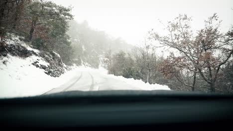 Driving-snowy-road-in-mountain-forest-in-winter,-windshield-view