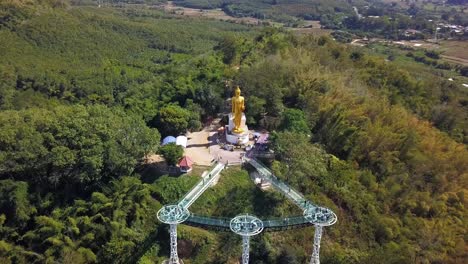 Golden-Buddha-Statue-Located-On-Top-Of-A-Hill-In-Chiang-Khan-Skywalk-Thailand---aerial-shot