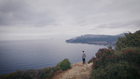 Man-at-the-edge-of-cliff-facing-peaceful-Mediterranean-Sea,-Marseille,-France