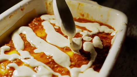 Adding-white-bechamel-sauce-in-lasagne-during-cooking-process,-still-shot
