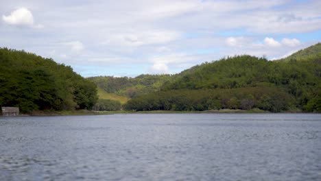 Agua-Que-Fluye-En-Un-Lago-De-Río-Tranquilo-Con-Tierras-Verdes-De-Bosques-Montañosos-En-Un-Día-Soleado-De-Verano