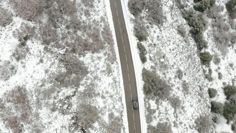 Top-down-aerial-view-on-black-car-driving-mountain-road-on-winter-day