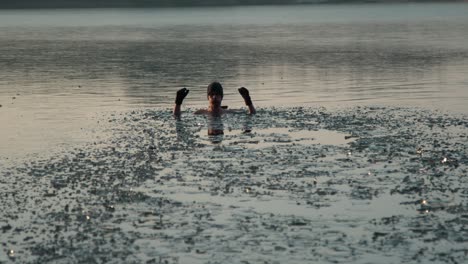 Ein-Junger-Mann-In-Einem-Zugefrorenen-See,-Der-Mit-Hohen-Händen-Ins-Wasser-Springt