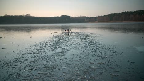 Ein-Junger-Mann-In-Einem-Zugefrorenen-See,-Der-Mit-Hohen-Händen-Ins-Wasser-Springt