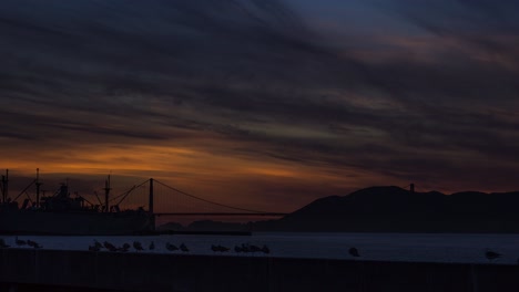 Schöner-Orangefarbener-Sonnenuntergang-In-San-Fransisco-Mit-Golden-Gate-Bridge-Im-Hintergrundsilhouet-Von-Möwen,-Zeitraffer