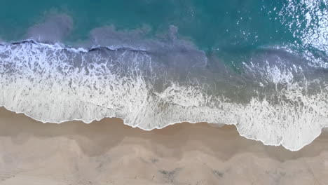Aerial-View-Of-Waves-Crashing-On-sandy-Beach-during-beautiful-summer-day