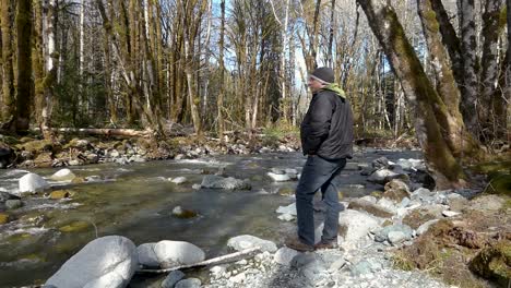 Man-walking-in-a-forest-looking-at-river-with-big-rocks-in-it