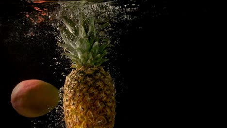 Ananas-Und-Mango,-Die-Langsam-In-Das-Klare-Und-Dunkle-Wasser-Fallen