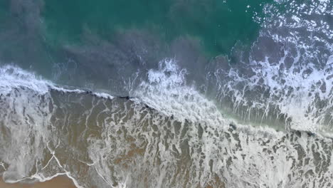 Aerial-top-down-shot-overhead-flying-along-a-beach-with-the-waves-rolling-in-during-the-afternoon