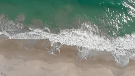 Slow-aerial-top-down-shot-of-crystal-clear-lagoon-beach-with-crashing-waves-in-Caribbean