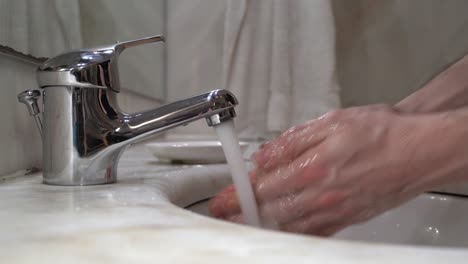 young-man's-hand's-are-washed-on-tap-water-with-soap,-then-rinsed-and-wiped-on-a-white-cloth-towel---side-view-close-up-static-shot-4k