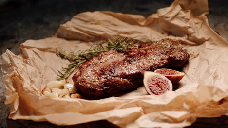 Juicy-gourmet-steak-presented-on-paper-with-rosemary,-figs-and-garlic-cloves