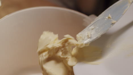 A-person-sliding-butter-with-a-silicone-spatula-into-a-bowl-in-slow-motion,-close-up-static