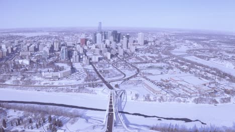 Aerial-rise-over-modern-developing-Winter-Snow-covered-city-in-downtown-Edmonton-Alberta-right-past-the-snow-coved-North-Saskatchewan-rivers-with-3-bridges-connecting