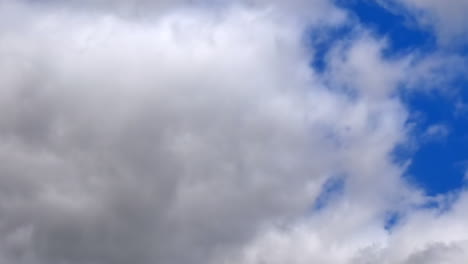 Zeitraffer-Von-Grauen-Und-Weißen-Dunklen-Regenwolken,-Die-Sich-Mit-Einem-Blauen-Fleck-Durch-Den-Himmel-Bewegen