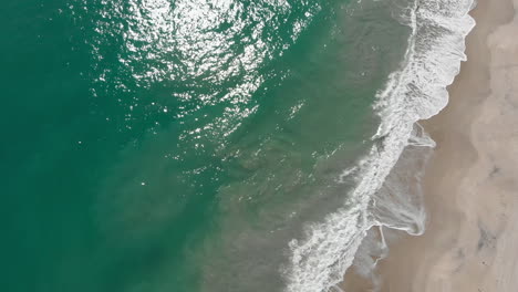 Aerial-top-down-shot-flying-along-a-beach-with-the-waves-rolling-in-during-the-afternoon