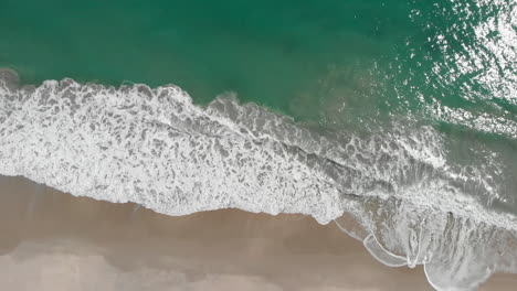 Top-Down-Aerial-View-Of-Azure-Blue-Water-and-Ocean-Breaking-waves-on-Sandy-Beach