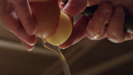 A-person-hands-cracking-open-a-egg-with-egg-white-and-yellow-yolk-pouring-out-in-slow-motion,-close-up