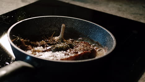 Cooking-steak-with-garlic-and-rosemary-in-pan-on-ceramic-stove