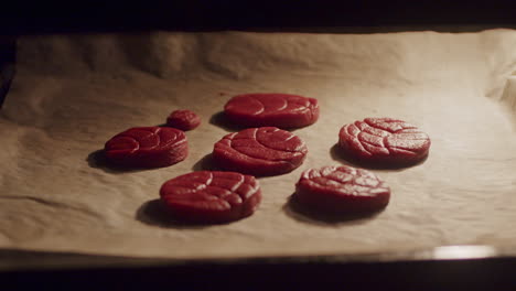 A-person-hand-putting-a-baking-sheet-inside-the-oven-with-raw-red-cookie-dough,-close-up