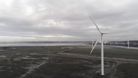 Sustainable-electrical-wind-turbines-spinning-on-England-farmland-descending-slow-push-in