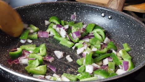 Cooking-green-peppers-and-red-onions-in-frying-pan-at-home,-closeup