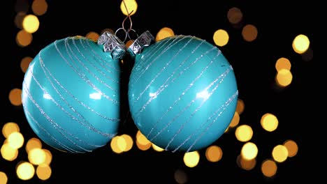 Zwei-Blaue-Türkisfarbene-Weihnachtskugeln-Mit-Glitzerstreifen-Und-Unscharfen-Lichtern,-Die-Im-Hintergrund-Flackern,-Nahaufnahme