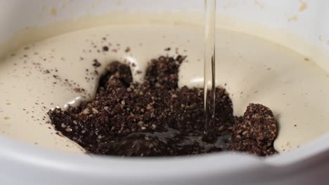 Machen-Sie-Einen-Glutenfreien,-Mehlfreien-Mandel-Schokoladenkuchen,-Gießen-Sie-Flüssiges-Kokosöl-In-Eine-Weiße-Schüssel-Mit-Geschlagenen-Eiern-Und-Trockenen-Zutaten-Wie-Gemahlenen-Mandeln-Und-Schokoladenstücken