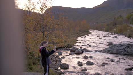 A-Woman-Takes-a-Photo-Next-to-a-Picturesque-River-in-Norway-in-the-Fall,-Slow-Motion