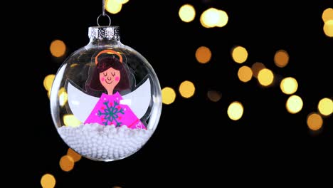 Einzelne-Klare-Weihnachtskugelverzierung-Mit-Karikaturdunklem-Haar-Engel-Und-Schnee-Innen-Unscharf-Lichter-Flackern-Im-Hintergrund,-Nahaufnahme
