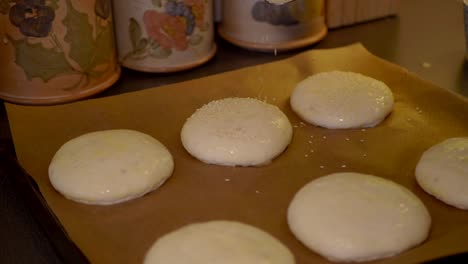 A-female-sprinkling-sesame-seeds-on-top-of-the-the-buns,-preparing-them-for-the-oven