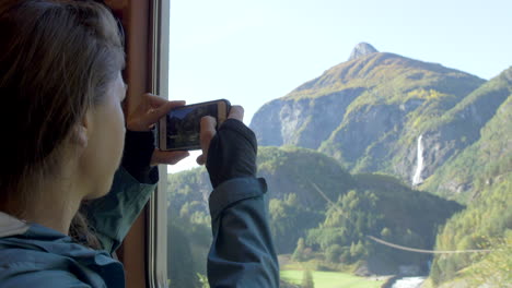 Eine-Frau-Fotografiert-Mit-Ihrem-Handy-Eine-Malerische-Berglandschaft-Vor-Einem-Zugfenster-In-Norwegen