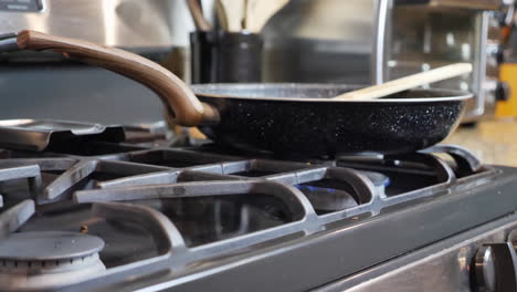 Pan-down-focus-of-cooking-pan-on-stove,-blurred-background-of-toaster-and-cooking-utensils