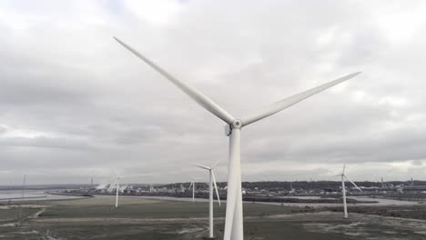 Sustainable-electrical-wind-turbines-spinning-on-England-farmland-close-left-aerial-orbit