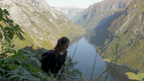 Eine-Frau,-Die-An-Einem-Sonnigen-Tag-In-Norwegen-Wandert,-Mit-Einem-Atemberaubenden-Blick-Auf-Einen-Fjord-Und-Die-Berge-Im-Hintergrund,-Zeitlupe