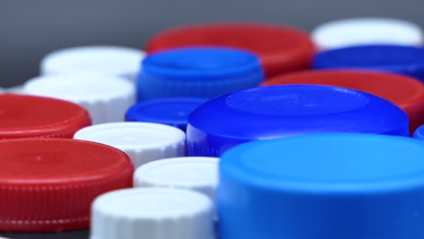 Gebrauchte-Kunststoffkappen-In-Rot-Blau-Weiß-Gefärbt,-Die-Sich-Vor-Einem-Grauen-Hintergrund-Schnell-Drehen