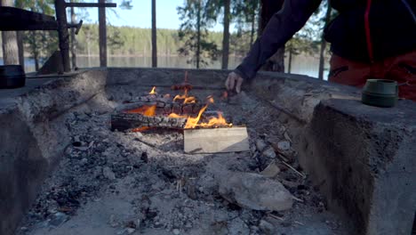 A-hiker-grilling-a-hot-dog-on-a-campfire-infront-of-a-small-lake