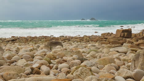 Storm-clouds-approach-as-tide-rolls-in-on-white-stone-beach-at-Cornwall,-UK