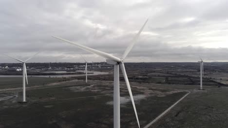 Nachhaltige-Elektrische-Windturbinen,-Die-Sich-Auf-Englands-Ackerland-Drehen,-Parallaxenumkreisen-Die-Rechte-Luftaufnahme