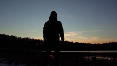 Young-silhouetted-man-wearing-hat-stops-and-looks-at-pretty-sunset
