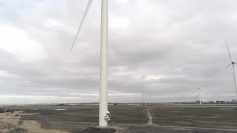 Sustainable-electrical-wind-turbines-spinning-on-England-farmland-rising-aerial-to-blades-rotating