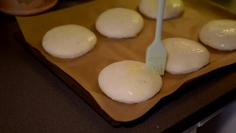 Close-up-of-a-female-brushing-wiped-egg-on-top-of-the-the-buns,-preparing-them-for-the-oven
