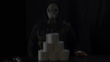 Man-with-gasmask-and-tactical-vest-putting-rol-of-toiletpaper-on-stack-of-toiletpaper