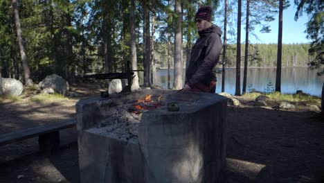 A-female-hiker-grilling-a-hot-dog-on-a-campfire-infront-of-a-small-lake