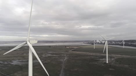 Sustainable-electrical-wind-turbines-spinning-on-England-farmland-static-aerial-view