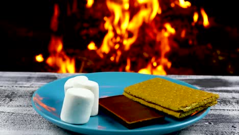 This-is-a-video-of-a-fire-burning-in-the-background-and-a-plate-with-the-ingredients-to-make-Smores