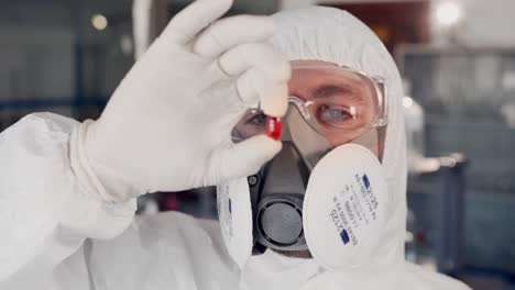 Nahaufnahme-Eines-Wissenschaftlers-In-Schutzanzug-Und-Atemschutzmaske,-Der-Die-Rote-Pille-Untersucht