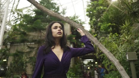 Young-attractive-indian-woman-is-walking-through-greenhouse-surrounded-by-greenery-touchin-the-tree-looking-around-slowmotion